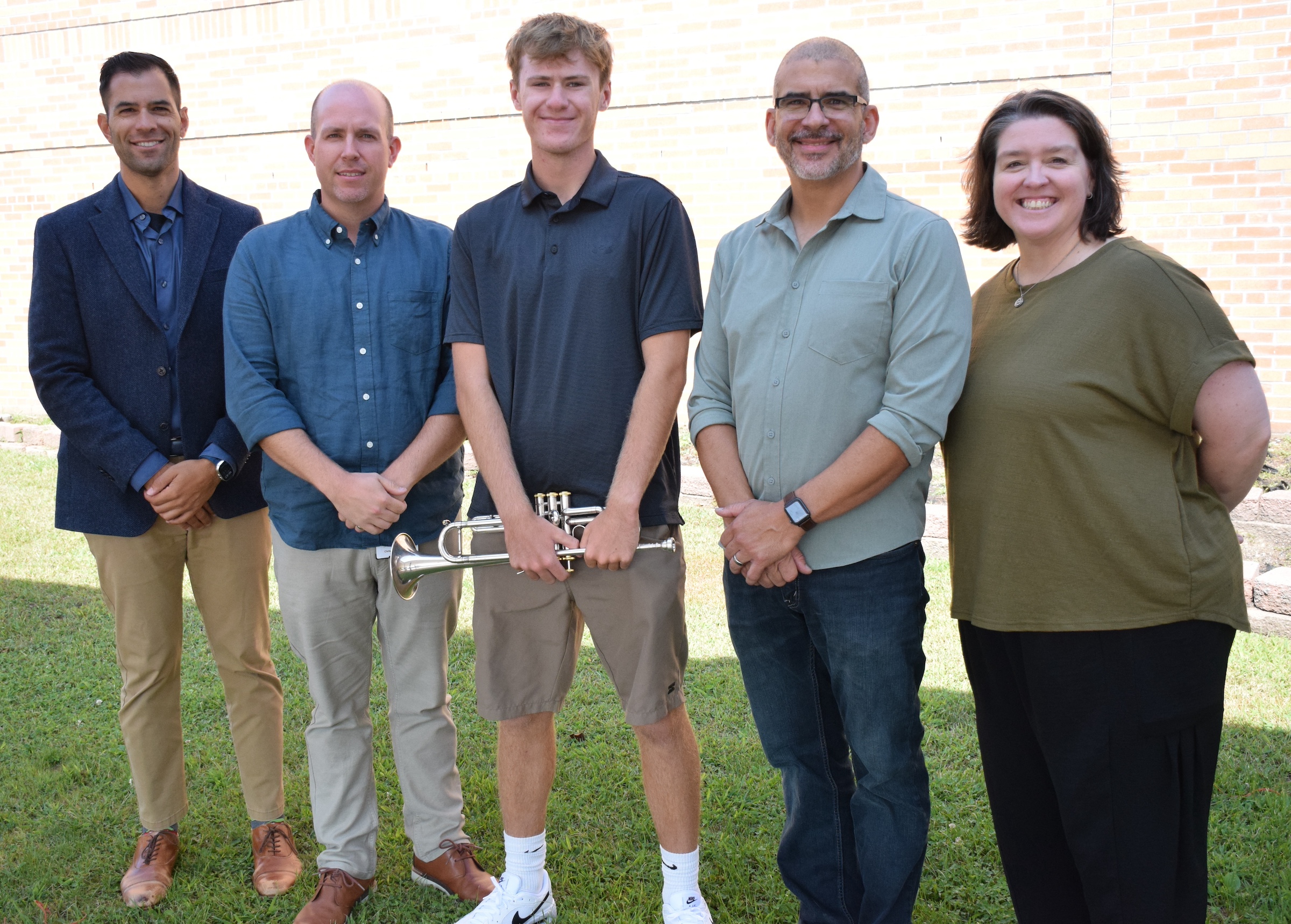 five people standing with student holding a trumpet